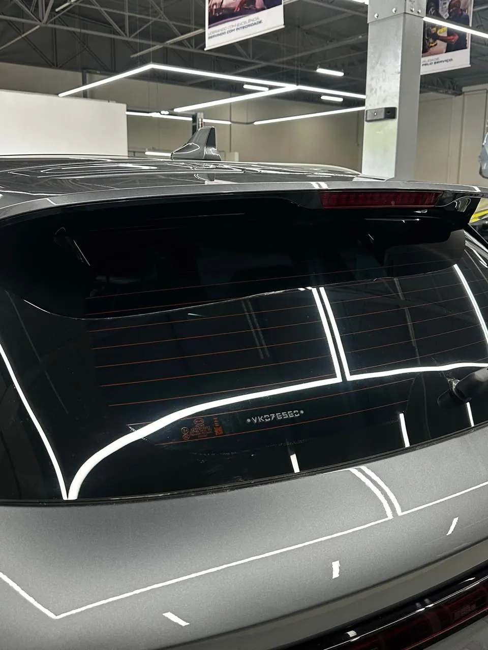 Vidro traseiro escurecido de SUV cinza, com reflexo das luzes da oficina